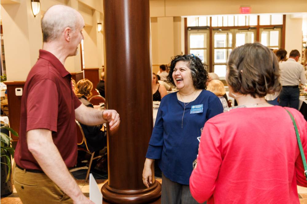 Dr. Samhita Rhodes (middle) smile in a conversation with attendees